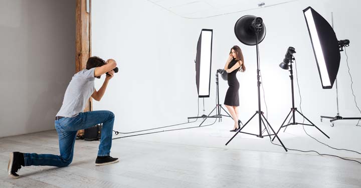 Fotógrafo de rodillas tomando fotos de una mujer rodeada de luces y un fondo blanco