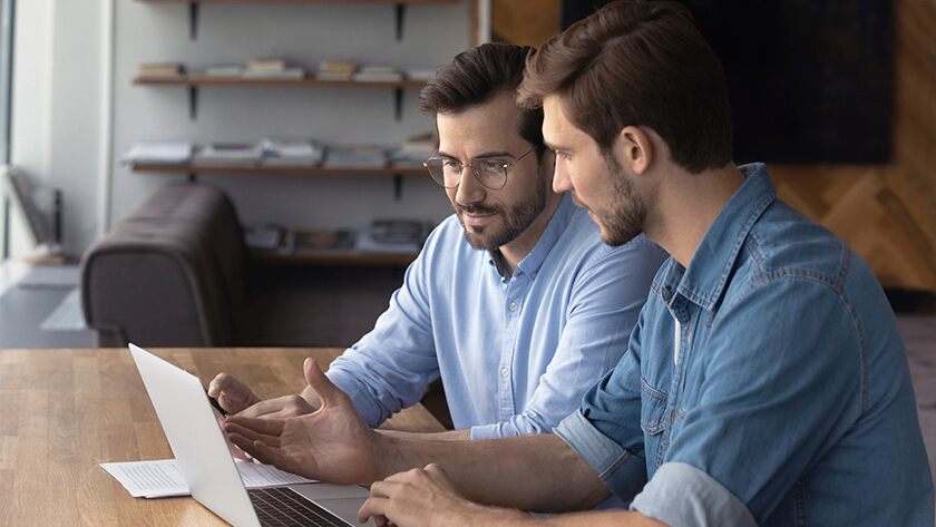 2 hombres en camisas de mezclilla mirando una computadora portátil y hablando