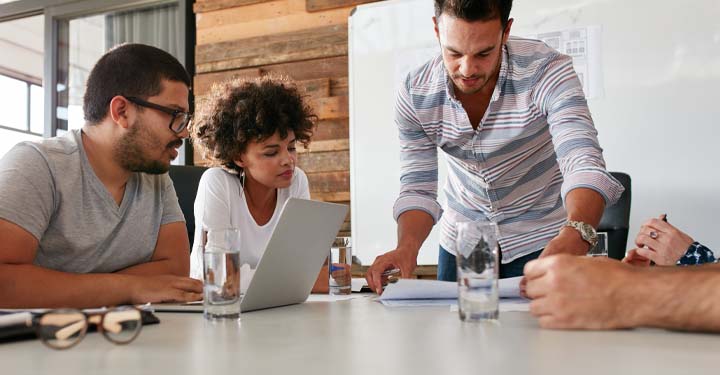 Compañeros de trabajo jóvenes que miran las computadoras portátiles y el papeleo en un escritorio