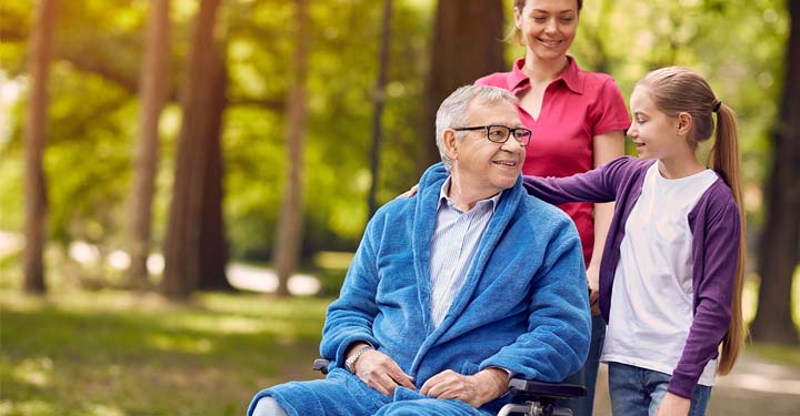 El abuelo y la nieta se sonríen en un parque mientras la madre de la niña empuja la silla de ruedas.