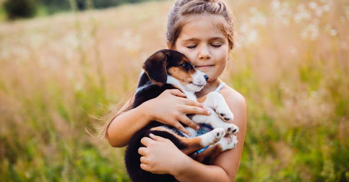Niña con los ojos cerrados felizmente sosteniendo un cachorro