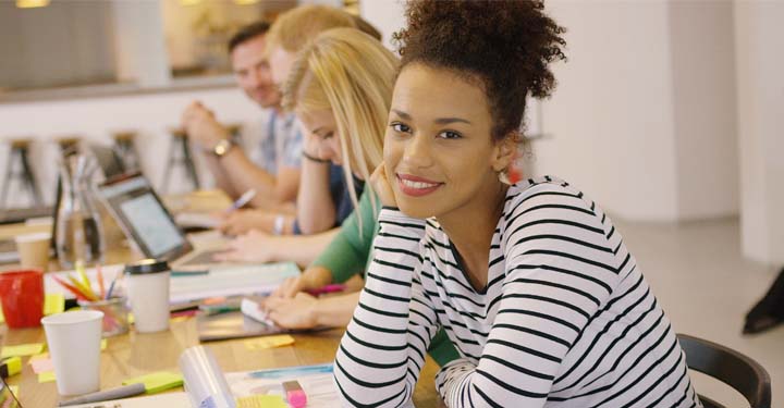 Mujer con camisa a rayas sonriendo a la cámara en el escritorio