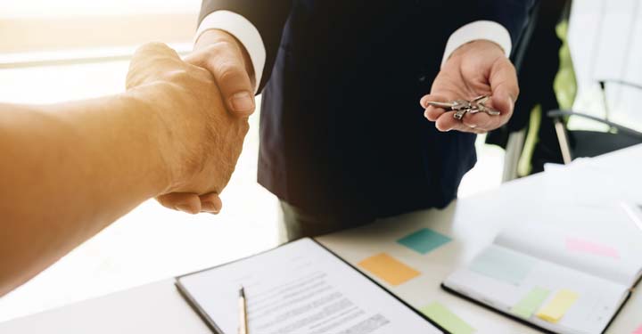 Gente dándose la mano y una entregando al otro un par de llaves