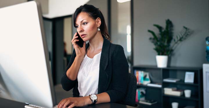 Empresaria en una oficina hablando por un celular y usando una computadora de escritorio