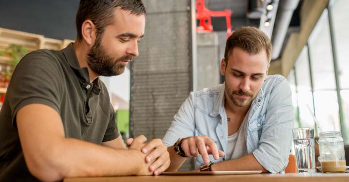 Dos hombres barbudos en un café miran el iPad