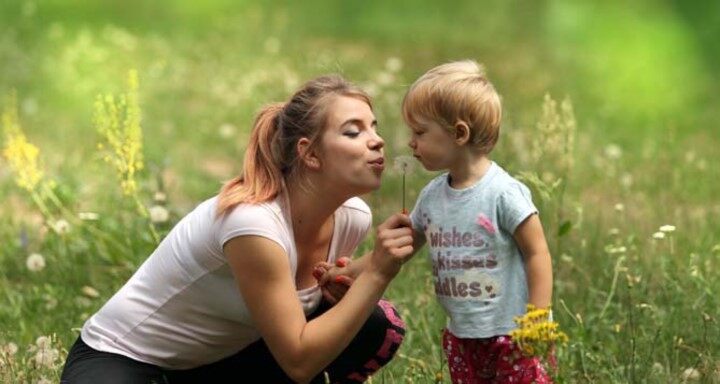 La mujer y el niño pequeño se sientan en un campo verde y soplan juntos un diente de león