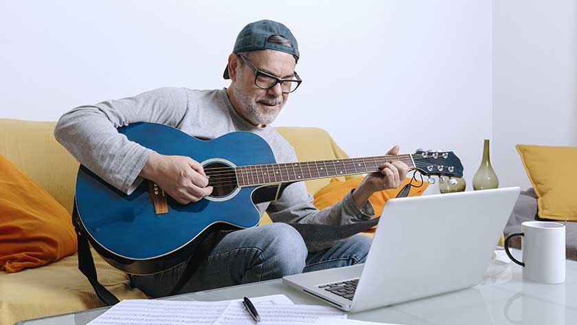 principal-tocando-la-guitarra-mirando-la-laptop-en-el-sofa