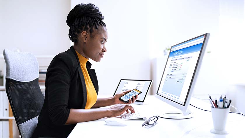 mujer-sonriente-sentada-en-el-escritorio-haciendo-banca-online