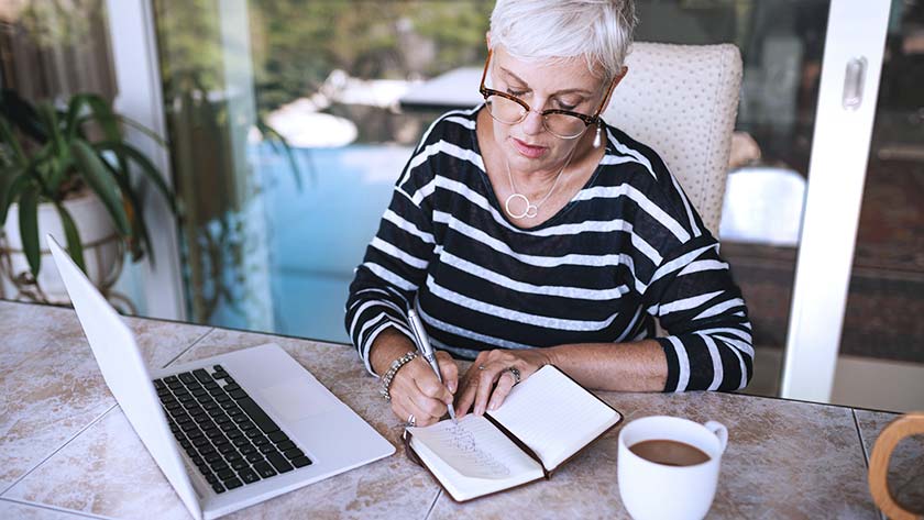 Senior mujer tomando notas de la computadora portátil