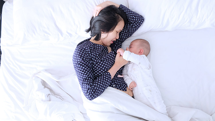 Lado de la mujer acostada en la cama con un bebé